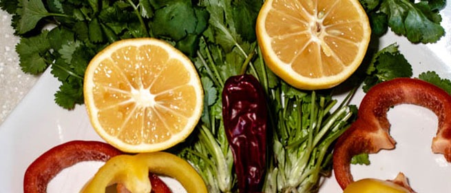 Нарезанные лимоны, кольца болгарского перца, стручок чили и пучок кинзы на белой тарелке.